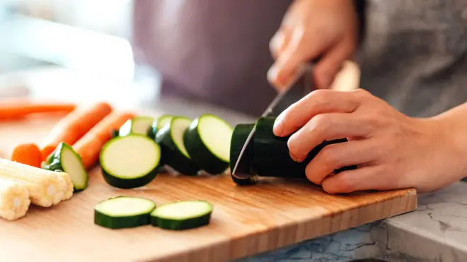 A person at home chops a courgette on a wooden chopping board