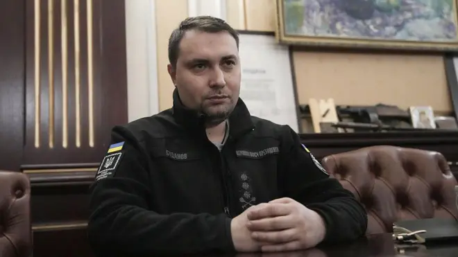 Кирило Буданов у чорній кофті сидить на шкіряному дивані в кабінеті, склавши руки на столі