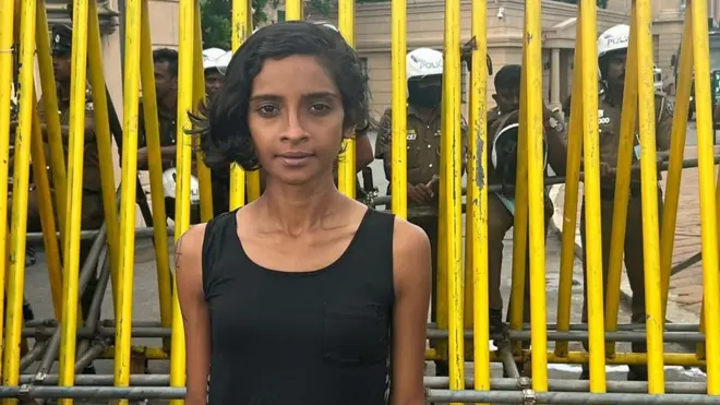 Melani Gunathilaka in front of railings with police behind her
