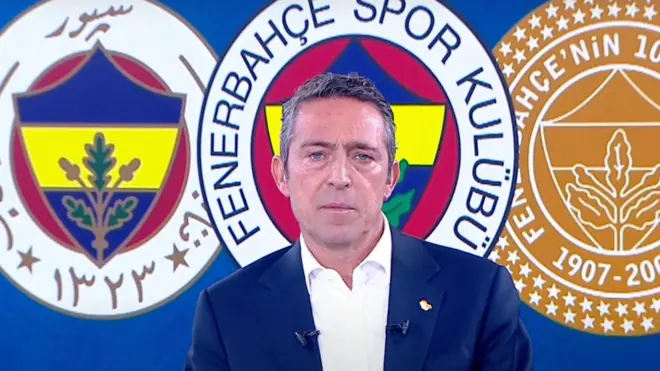 Ali Koç, Fenerbahçe logoları önünde açıklama yapıyor ve oldukça ciddi bir yüz ifadesi var. Takım elbisesinin kravatı yok