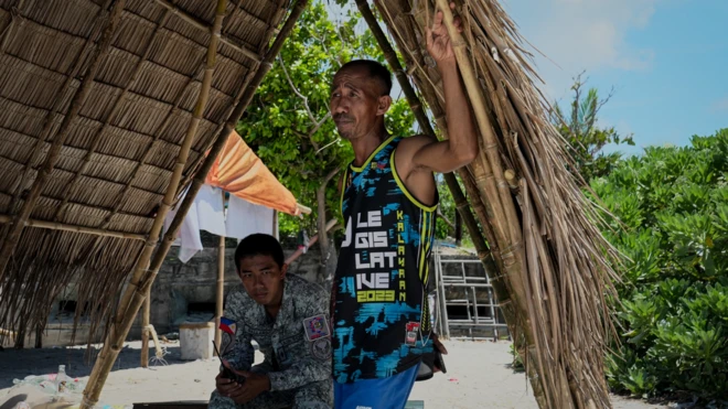 兩名男子站在蘆葦棚的陰涼處