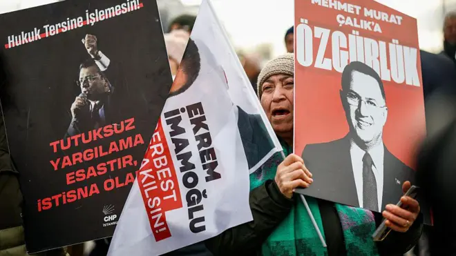 Ekrem İmamoğlu ve diğer sanıkların posterlerini tutan kalabalık. Bir kadın slogan atıyor.