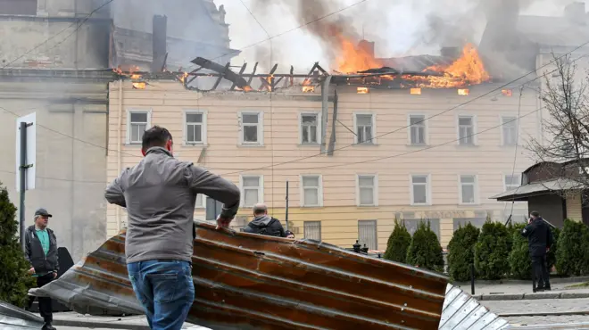 A man clears debris as a building burns in the background after Russian strikes on Lviv on Tuesday