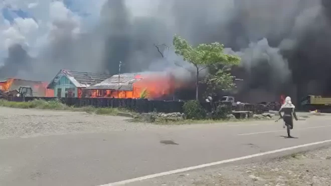 Seorang pria sedang berlari di jalan sambil menengok ke bangunan yang terbakar.