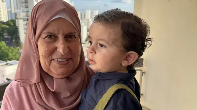 Senhora com véu islâmico e bebê no colo; ao fundo, prédios de São Paulo