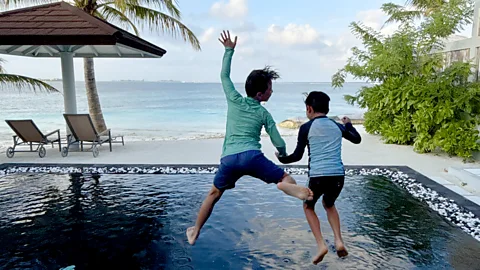 Two boys jumping into swimming pool in the Maldives with ocean behind (Credit: Carmen Roberts)