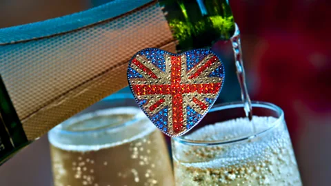 A bottle pouring out champagne into two glasses, with a heart-shaped Union Jack flag in the centre of the frame (Credit: Alamy)