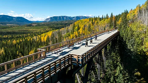 A scenic view of people cycling or walking across a historic railway trestle above a deciduous forest (Credit: Peter O'Hara/ Travel Alberta)