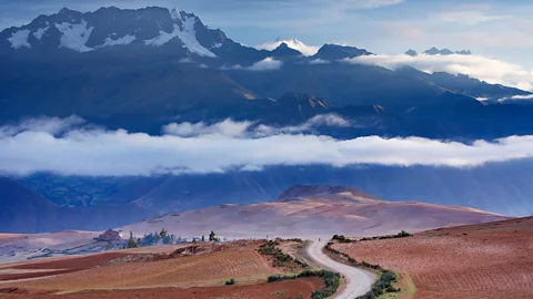 A curved road heading into the distance with mountains and clouds in the background (Credit: Alamy)