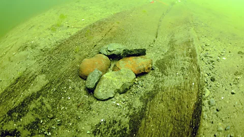 Rocks on top of a sunken ancient canoe under greenish waters (Credit: Wisconsin Historical Society)