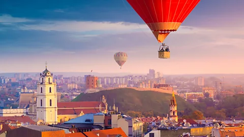 Hot air balloons floating above Vilnius Old Town with church tower, red rooftops and Gediminas Hill visible below (Credit: Getty Images)