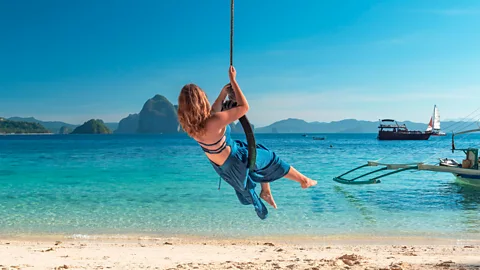 A woman swings on a vine into the water at El Nido Beach in the Philippines (Credit: Alamy)