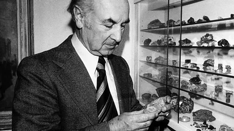 Black-and-white photo of Albert Hofmann in a suit and tie examining a collection of rocks on a shelf in 1976 (Credit: Getty Images)