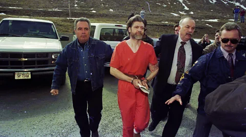 Getty Images Theodore Kaczynski, the Unabomber, dressed in an orange prison jumpsuit and handcuffed, being led by federal agents (Credit: Getty Images)