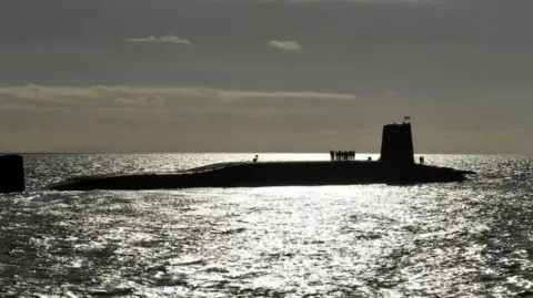 A wide shot of a submarine at water level. The sun has gone down and is glistening on the sea.