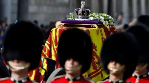 The coffin of Queen Elizabeth II, draped in the Royal Standard with the Imperial State Crown placed on top, is carried along Whitehall on a horse-drawn gun carriage of the King's Troop Royal Horse Artillery, during the ceremonial procession from Buckingham Palace to Westminster Hall, London, where it will lie in state ahead of her funeral on Monday. Picture date: Wednesday September 14, 2022.