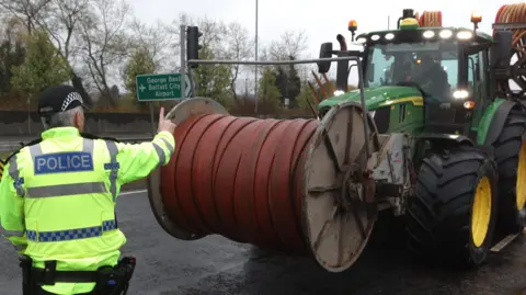 A PSNI officer standing in front of a tractor on a road in Belfast 