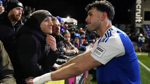 Macclesfield's Sam Heathcote is consoled by fans after his own goal settled the FA Cup fourth round tie against Brentford.