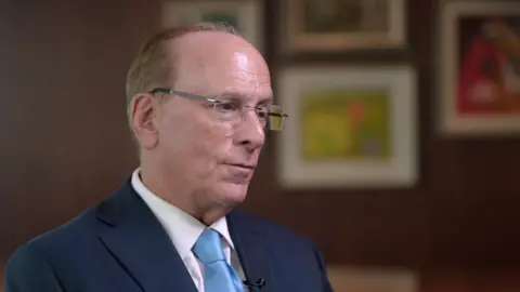 Blackrock CEO Larry Fink being interviewed. He is wearing a dark blue suit, white shirt and light blue tie