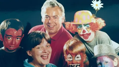 Paul and Lauren Staton pictured in the middle of four children who have their faces painted in bright colours. 
