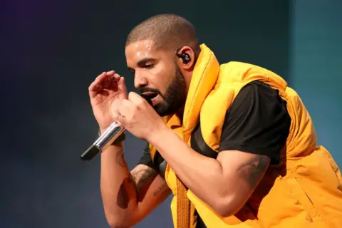 Getty Images Drake performs on stage, wearing a yellow bomber jacket over a black t-shirt