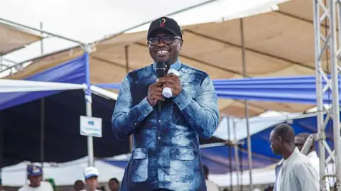 AFP via Getty Images Benin s Finance Minister Romuald Wadagni in a blue shirt and a black cap, holding a microphone