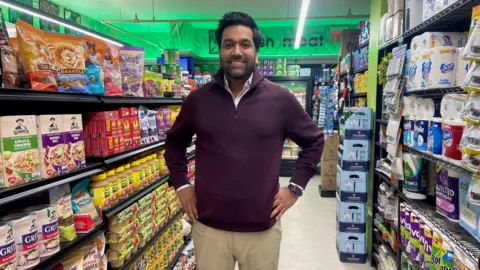 Alap Vora stands in the aisle of his grocery store in New York