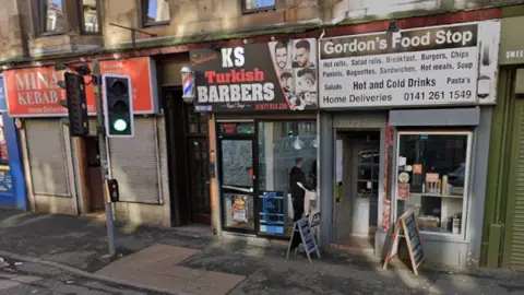 Google Exterior of KS Turkish Barbers alongside other shops, taken in 2022. There are flats above.