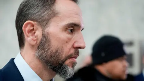 Smith arriving for his testimony wearing a suit and surrounded by journalists and security staff