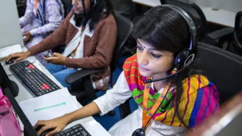 Employees wear headsets while working at the Avise Techno Solutions LLP call center in Kolkata, India, on Sunday, Dec. 24, 2017.