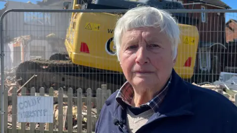 Edd Smith/BBC Bryony Nierop-Reading, a woman standing in front of her house which is being demolished. She is looking directly at the camera.