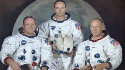 NASA Official portrait of the Apollo 11 crew Neil Armstrong, Michael Collins and Buzz Aldrin, dressed in their spacesuits, taken against the backdrop of an image of the Moon