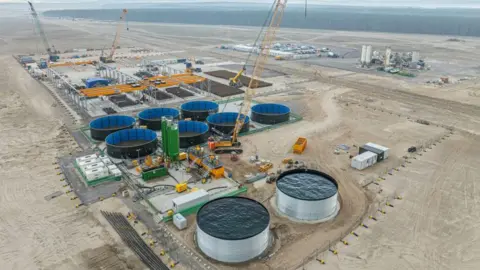Construction at Ardersier Port. The site is flat and sandy and there are a number of large structures including circular tanks.