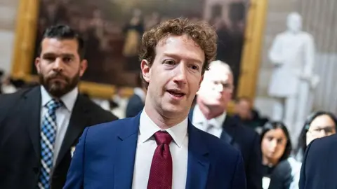 Mark Zuckerberg wearing a blue suit and red tie, walking through the Capitol. 