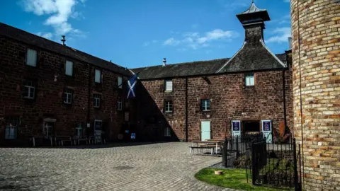 Getty Images A traditional red brick building surrounds a courtyard. There are green shutters on the doors and windows, and a Saltire hanging from the roof. 