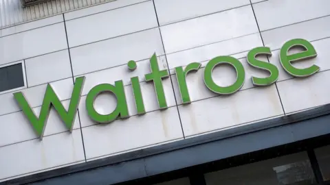 A sign above a door of a supermarket. It is in a light green font and reads: Waitrose