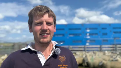 A young man with brown hair and a blue top.