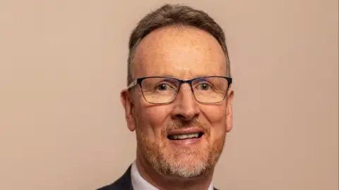 Rev Richard Kerr wears square glasses and has short ginger and grey stubble