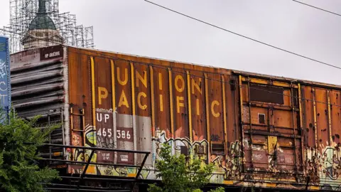 A rust-orange intermodal container with graffiti and the Union Pacific label sits on an overpass near the Union Pacific Railroad Global 1 rail yard in Chicago, Illinois, US, on Friday, July 25, 2025.