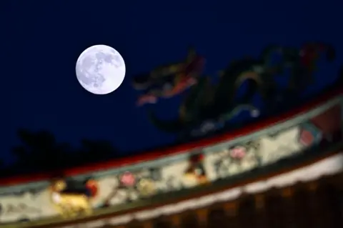 Getty Images The supermoon lights up against a black blue sky, in focus, above an out-of-focus red and white building.